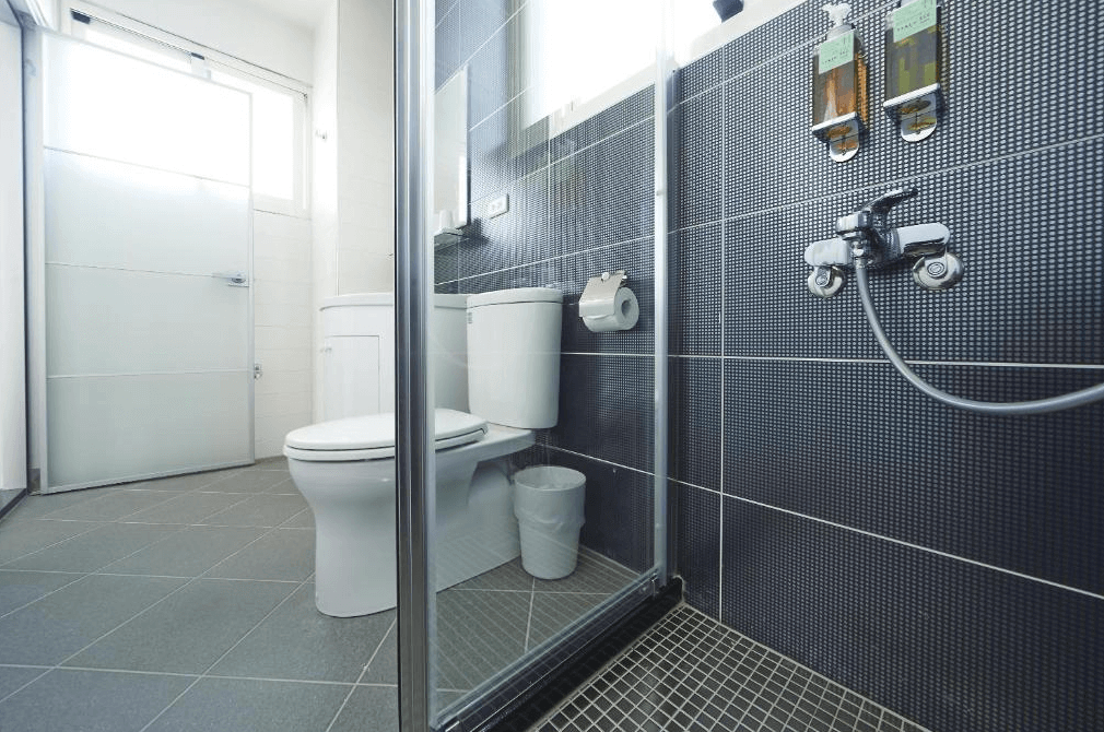 好漾民宿youngstay的衛浴空間，牆面使用深色小磚裝飾，淋浴間使用玻璃隔間。衛浴設備齊全，整體設計簡潔時尚，地板和牆面搭配展現出現代感。