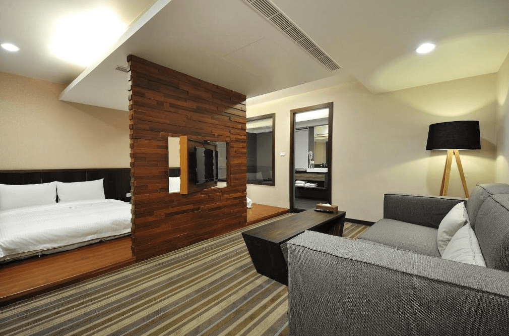 山水商務飯店的套房，設有木質隔間牆，分隔出睡眠區與休憩區。客廳內有灰色沙發和木質茶几，整體風格現代簡約，營造出舒適的氛圍。
