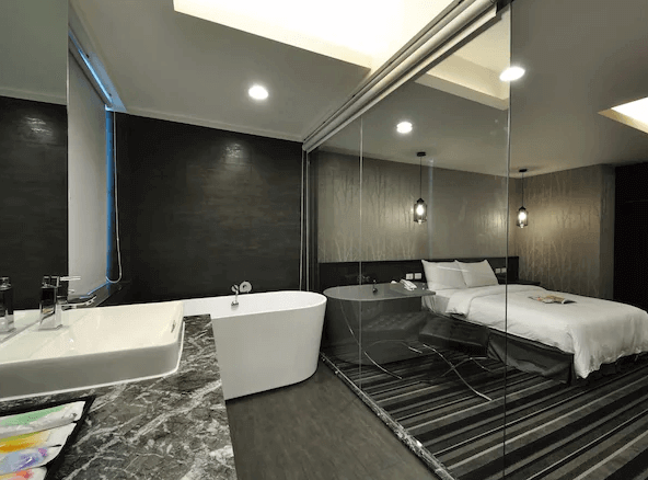 山水商務飯店的黑白色調現代套房，浴室區域設有白色的獨立浴缸和大理石檯面，並以透明玻璃隔開睡眠區，呈現時尚的設計感。