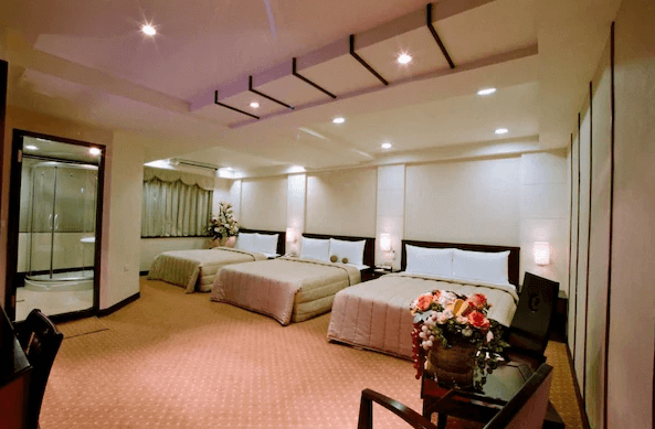 山水商務飯店寬敞的家庭房，內有三張雙人床，並配有花藝裝飾。房間空間寬敞明亮，適合多人住宿，床鋪配置整齊，營造出溫馨的氛圍。