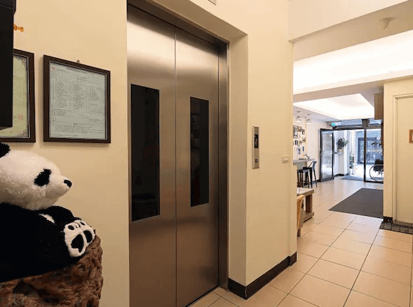 幸福YES民宿三館的電梯區域，旁邊放置了一個熊貓玩偶，營造出溫馨的迎賓氛圍。走廊空間寬敞明亮，通往大廳與其他設施。