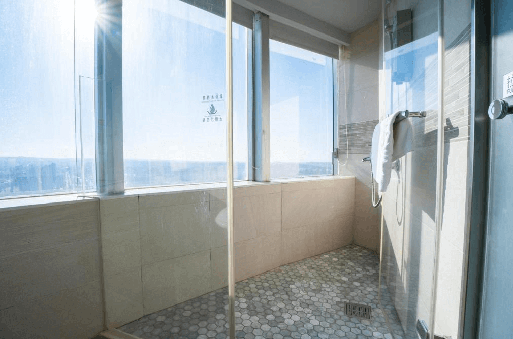 新舍商旅中壢館的浴室，採用六角形瓷磚地板設計，牆面及地板均以淺色調為主，淋浴區設有透明玻璃隔間及毛巾架，大面落地窗提供開闊的視野與自然光線。