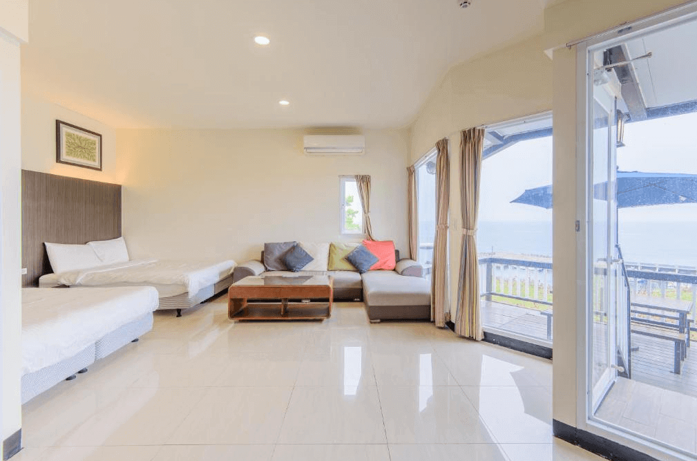 【小琉球住宿】杉福海灣渡假會館的海景客房，內設兩張床與一組L型沙發，窗外直通陽台，可以欣賞戶外的海景與藍天，整體空間明亮且簡約。
