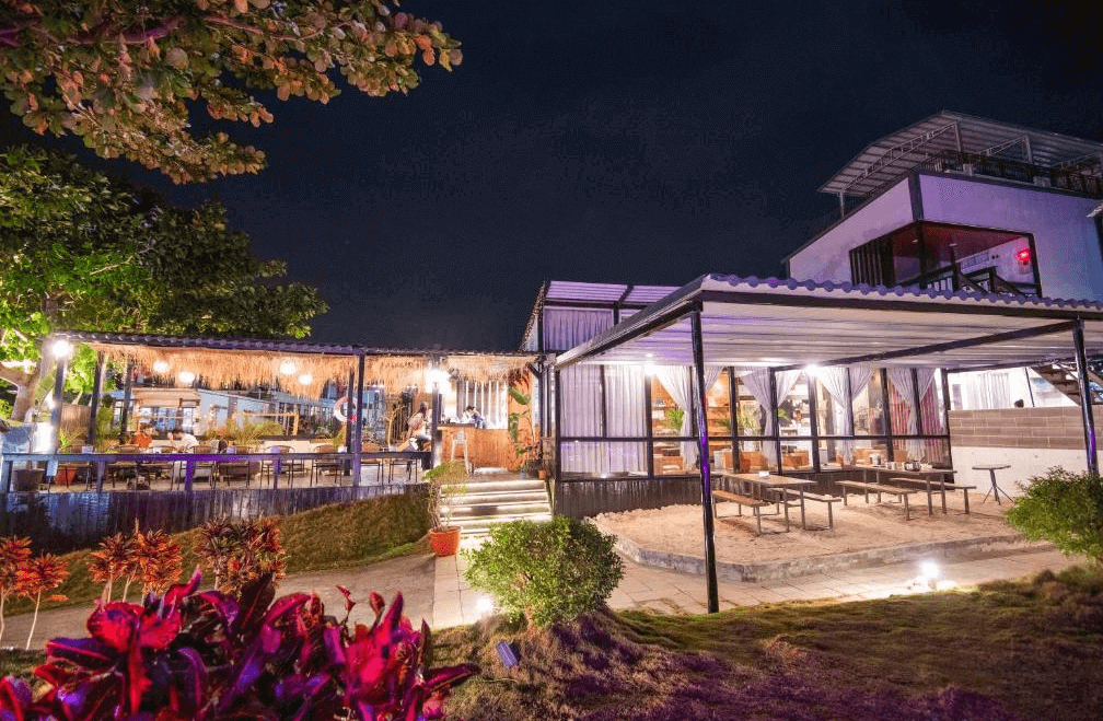 【小琉球住宿】杉福海灣渡假會館的夜晚戶外餐廳空間，設有稻草屋頂與柔和的燈光，庭院以熱帶植物點綴，提供一個溫馨且適合聚餐的環境。