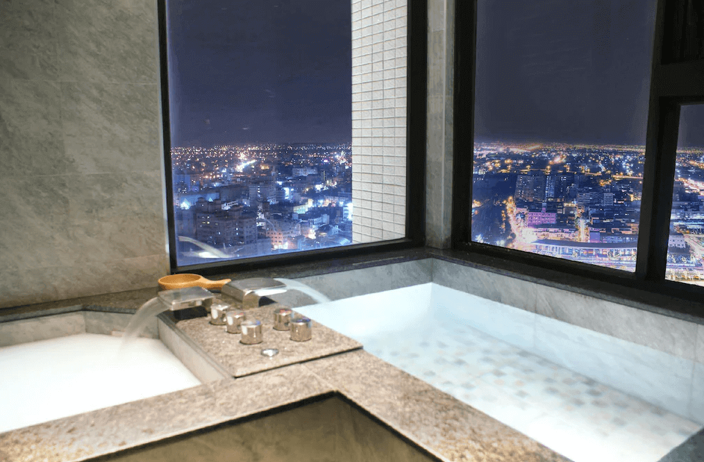 村却國際溫泉酒店的溫泉浴池特寫，設置在一處高樓，可俯瞰城市夜景。浴池的水龍頭設計時尚，浴池邊緣以大理石材質包覆，營造出高級的質感。
