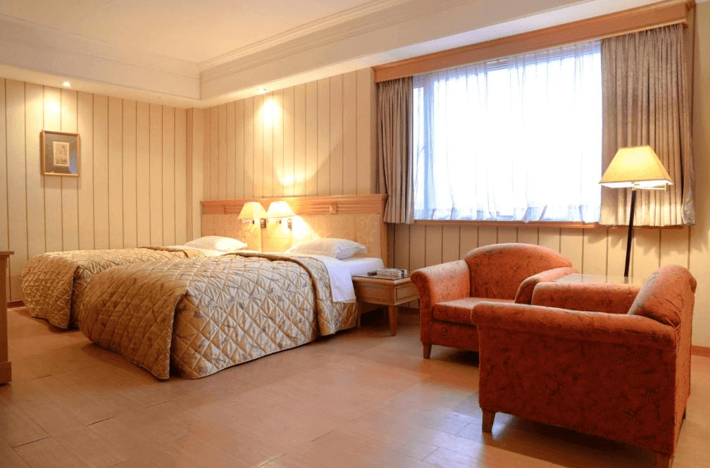 【新營汽車旅館】歐堡商務汽車旅館溫暖典雅的雙人房設計，採用柔和的木質調，配有兩張單人床和舒適的座椅區，窗戶提供自然光線，營造出溫馨的居住氛圍。