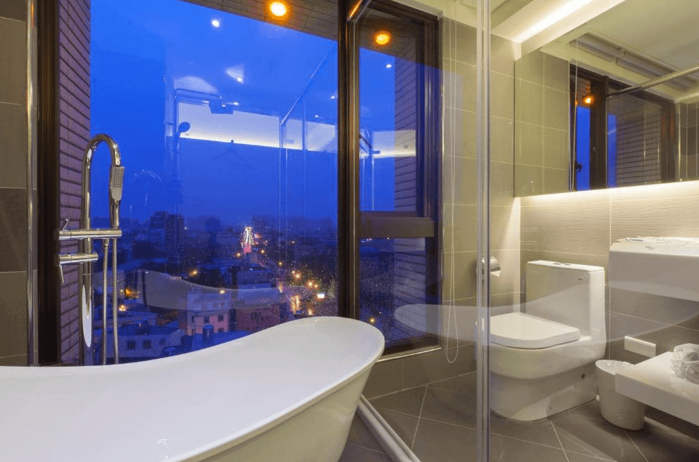 【中壢火車站住宿】“中壢夜市住宿”沐楓商旅的浴室，內設有獨立浴缸及淋浴間，並以大面積落地窗呈現城市夜景，營造出放鬆愜意的氛圍。