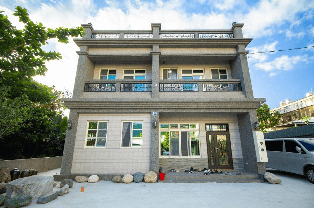 田媽媽民宿三層樓的建築外觀，牆面為灰白色調，設有黑色陽台欄杆，門口放置石頭與植物，增添自然氛圍。
