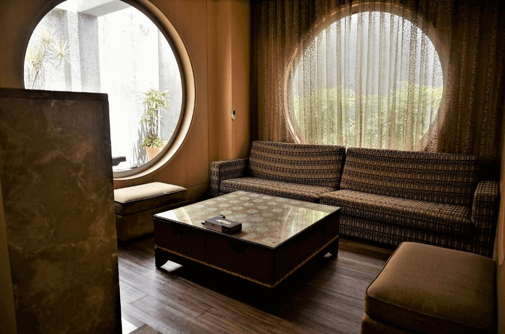 【新營汽車旅館】禾楓水舍汽車旅館圓形窗戶旁的休息區，配有舒適的沙發和茶几，窗外的綠意景色提升房間的自然氛圍。
