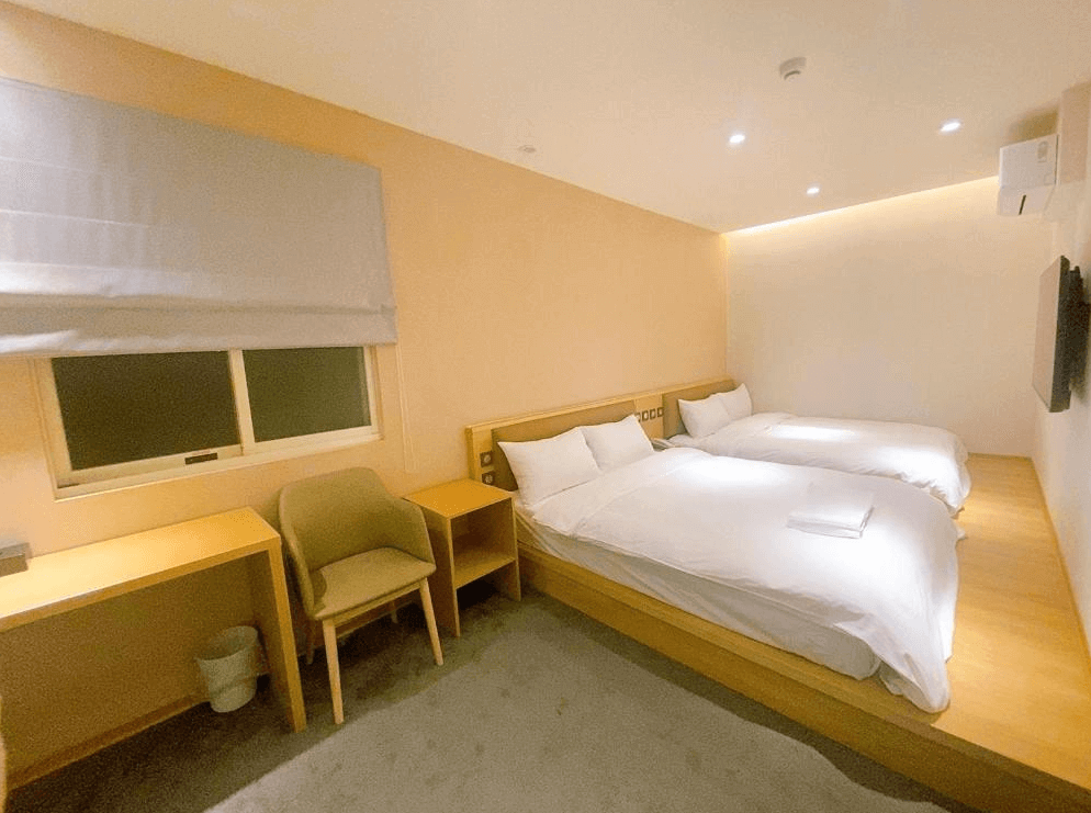 【中壢火車站住宿】“中壢夜市住宿”米淇旅店中壢館的客房，內有兩張雙人床，木質床架與家具搭配柔和的燈光，牆壁採用淺色系設計，房內設有書桌與椅子，整體氛圍舒適且放鬆。