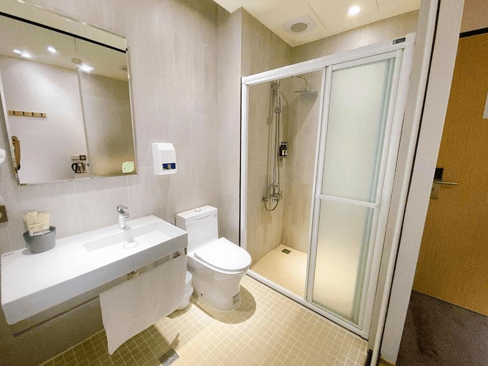 【中壢火車站住宿】“中壢夜市住宿”米淇旅店中壢館整潔的浴室，內設淋浴間、馬桶及洗手台，淋浴間以磨砂玻璃隔開，牆面與地板均採用淺色瓷磚設計，提供明亮且乾淨的使用空間。