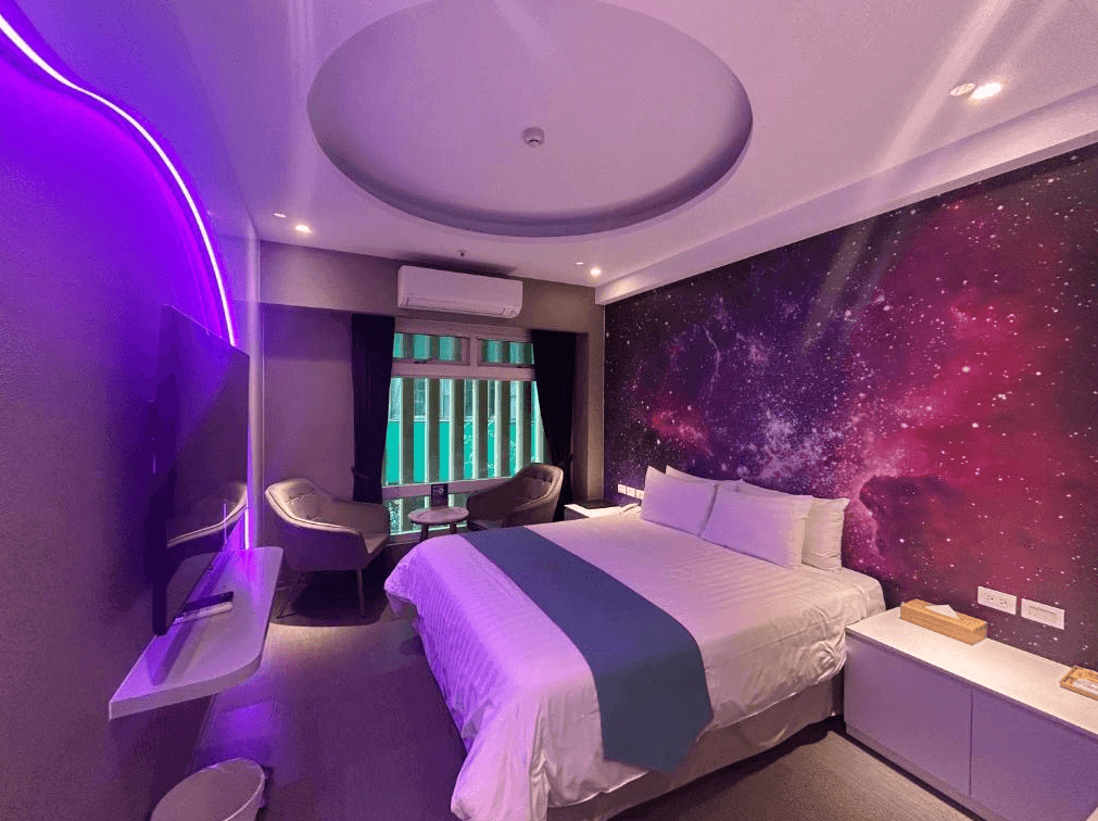 賓利酒店富有科技感的客房，牆面設計為宇宙星空圖案，搭配紫色氛圍燈，房內有一張雙人床，旁邊設有小型圓桌與兩張單椅，營造出浪漫且神秘的氛圍。
