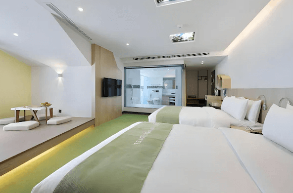 雀客童媽吉親子旅館的溫馨雙床房，設有日式榻榻米區和簡單的矮桌，整體風格以淺色為主。房間內的浴室以透明玻璃隔開，讓空間顯得更寬敞明亮。