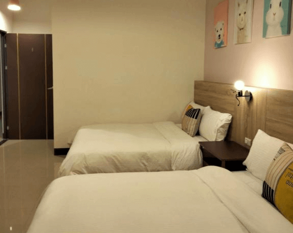【玉里住宿】910 hostel 城東館的雙人房，設有兩張雙人床，床頭櫃上有簡單的壁燈。牆上掛有三幅以可愛動物為主題的裝飾畫，房間乾淨整潔，採用簡約風格設計。