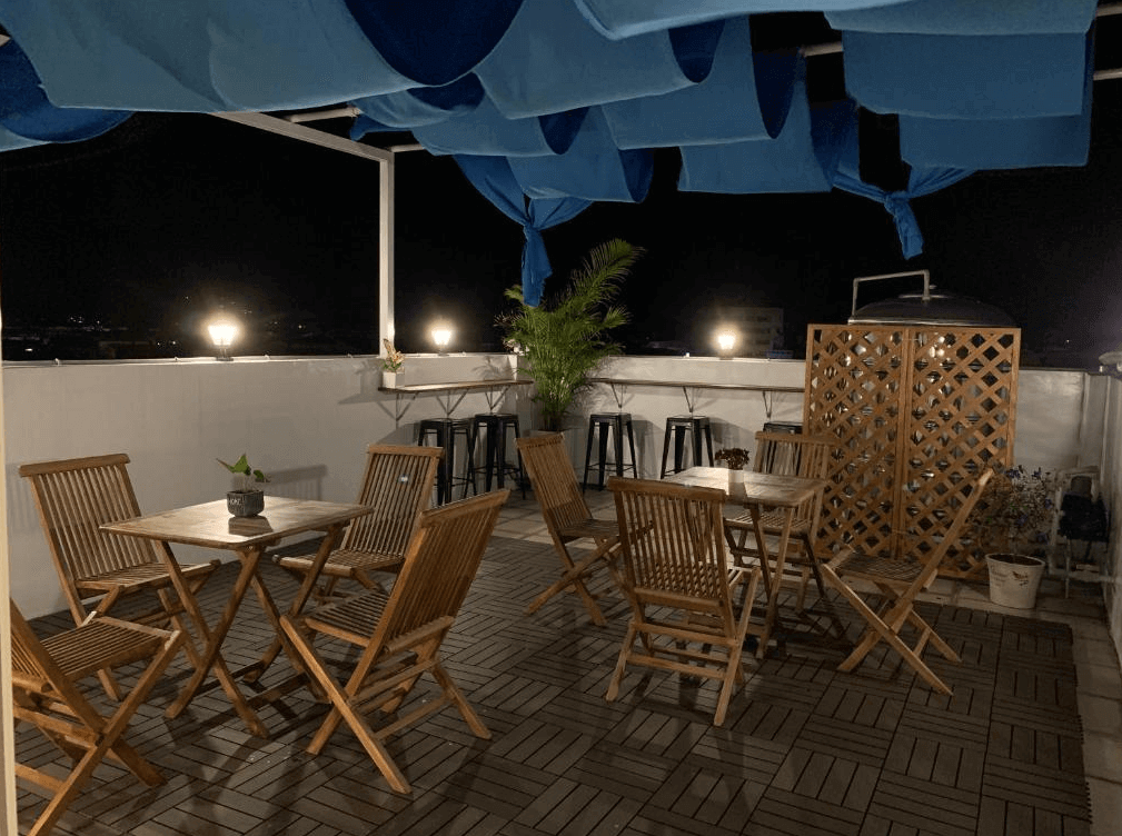 【玉里住宿】910 hostel 城東館的戶外露台，設有多組木製桌椅，天花板懸掛藍色布簾，營造溫馨的氛圍。夜晚的燈光柔和，適合聊天或放鬆。