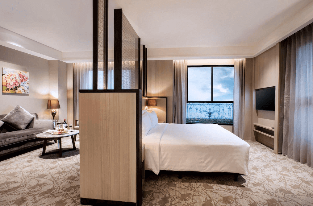 【礁溪住宿】中天溫泉渡假飯店的雙人房，設有分隔屏風區分臥室與起居空間，房間內採用柔和米色調搭配地毯，窗外景致開闊，增添入住的溫馨與放鬆感。