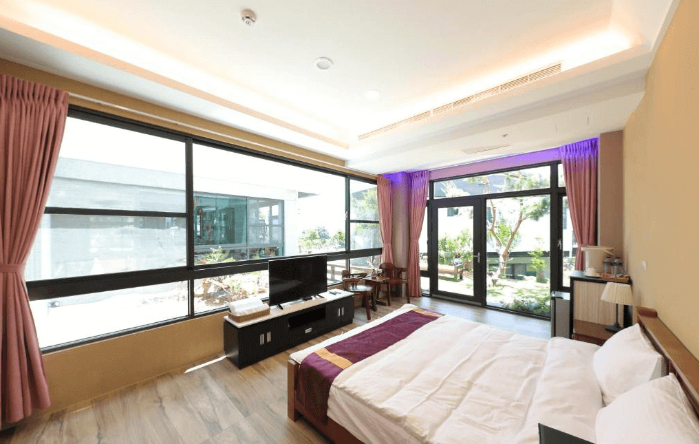 【水里住宿】五山三水莊園民宿的臥室，設有大片落地窗與玻璃門，讓自然光灑滿整個空間，窗外能夠欣賞庭園景色。房間內設有木質地板、大床、電視，以及簡潔大方的擺設，營造舒適的住宿氛圍。
