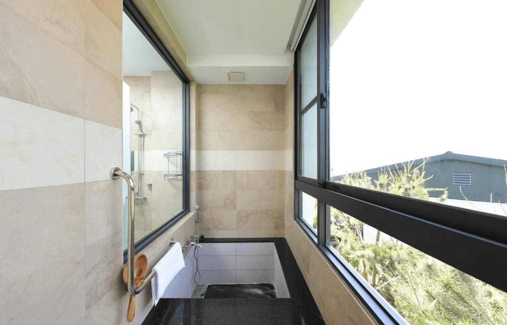 【水里住宿】五山三水莊園民宿的窗景浴室，設有小型泡澡池與淋浴設備，牆面採用淺色石材設計，簡潔且高雅。透明玻璃窗讓住客在享受放鬆時也能欣賞戶外的綠意景觀。
