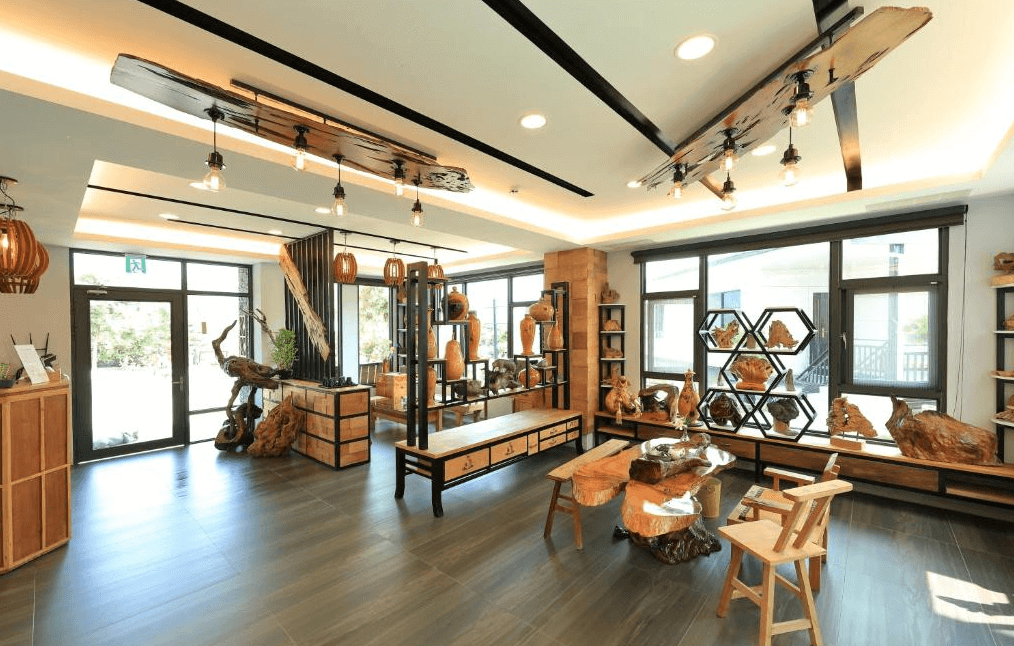 【水里住宿】五山三水莊園民宿的公共空間，設計以原木風為主題，搭配工業風吊燈，展現溫暖與個性兼具的風格。展示櫃中陳列著手工木雕工藝品，空間充滿文化與藝術氣息，是交流或放鬆的好地方。