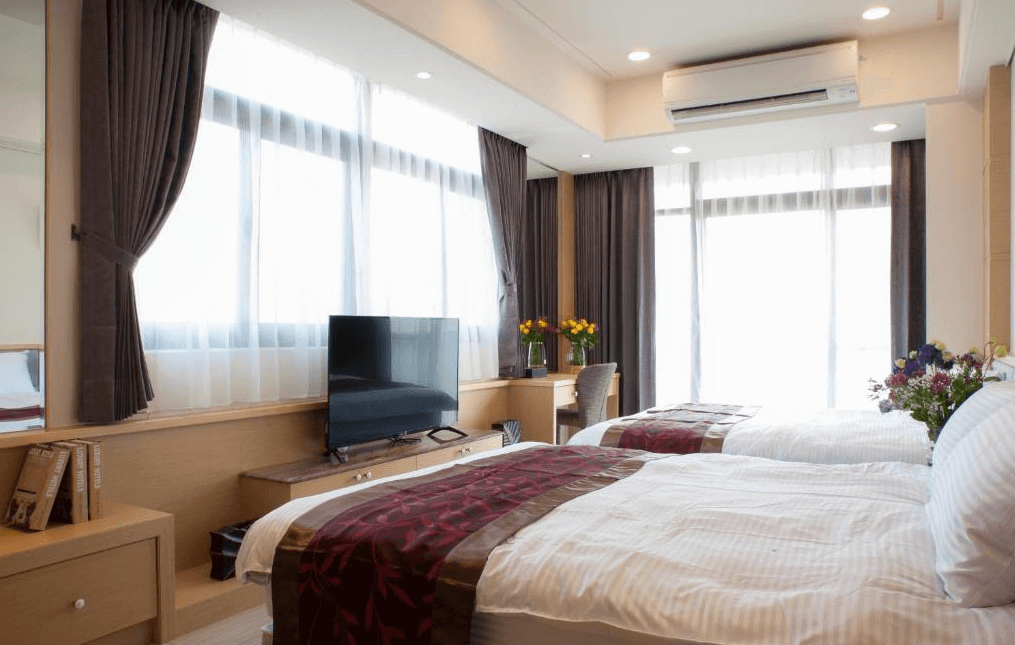 【水里住宿】八台莊園民宿的雙人床溫馨臥室，房間採用柔和的淺色調設計，搭配深色窗簾，營造出舒適且放鬆的氛圍。窗邊設有桌椅與擺放鮮花的裝飾，充滿溫馨氣息。