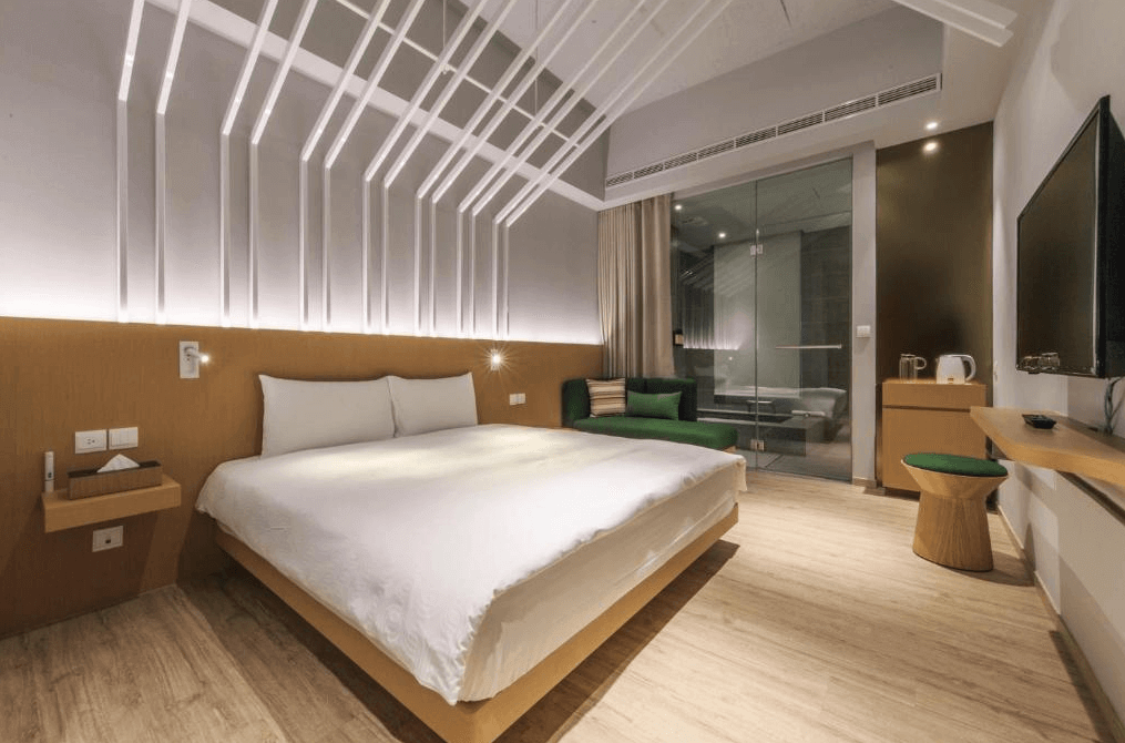 【礁溪住宿】品文旅礁溪的雙人房，配有一張大床，牆面以立體白色線條裝飾，搭配木質地板與家具，房內設有綠色沙發，玻璃門外連接寬敞的浴室空間。