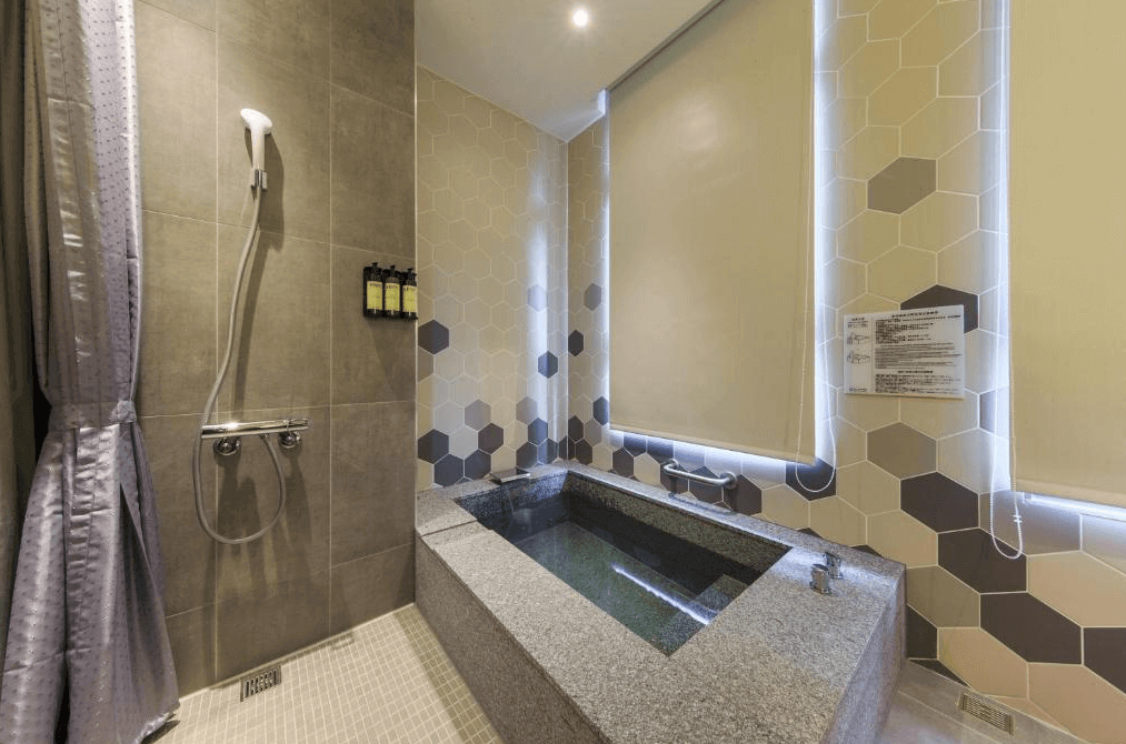 【礁溪住宿】品文旅礁溪的浴室內設有淺灰色六角磚牆面與深色石材浴池，窗簾拉上後保持隱私，另附有淋浴設備與高品質的沐浴用品。