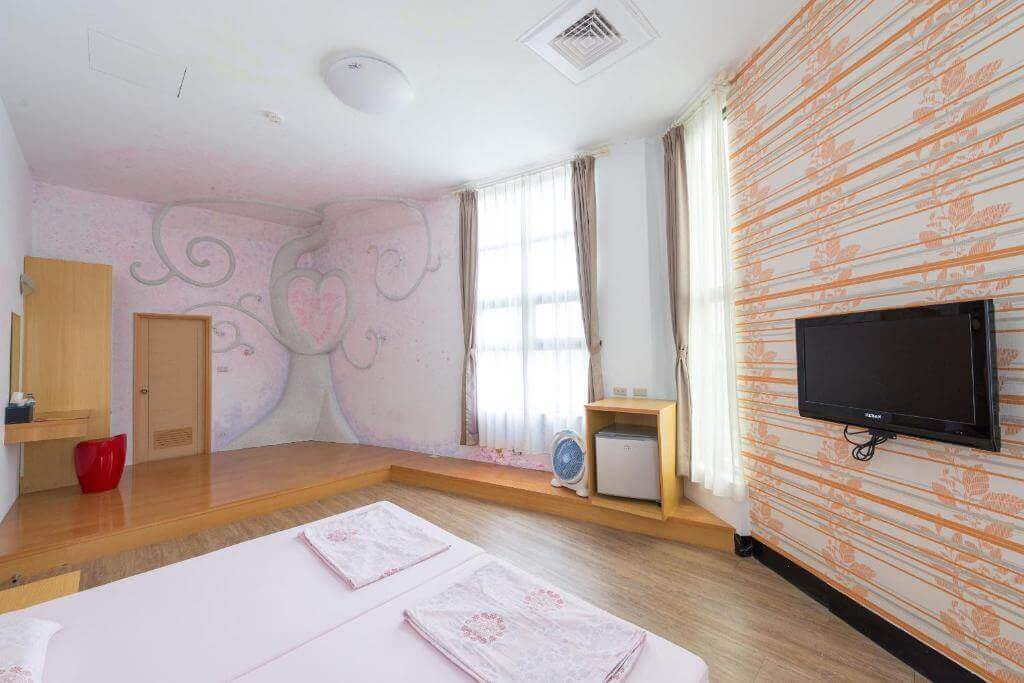 【北港住宿】好住民宿的房間設計採用溫馨的粉色與木質調，牆面繪有童話風格的愛心樹圖案，搭配大片窗戶提供充足的自然光線，營造出明亮且浪漫的氛圍。