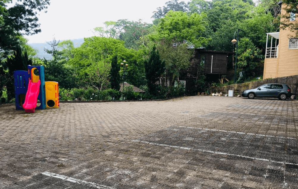 【通霄住宿】如意園民宿民宿寬敞的戶外停車場，周圍環繞著綠樹，設有多個停車位。角落有五彩繽紛的兒童遊樂設施，包括滑梯，適合親子家庭入住時讓孩童遊玩。