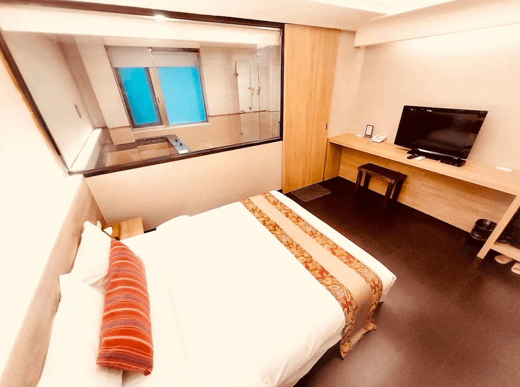 【烏來住宿】山水妍溫泉會館的房間內部設計溫馨舒適，配有一張大床、平板電視、木質書桌，玻璃隔間浴室設計讓空間感更寬敞，木質與簡約風格相得益彰。