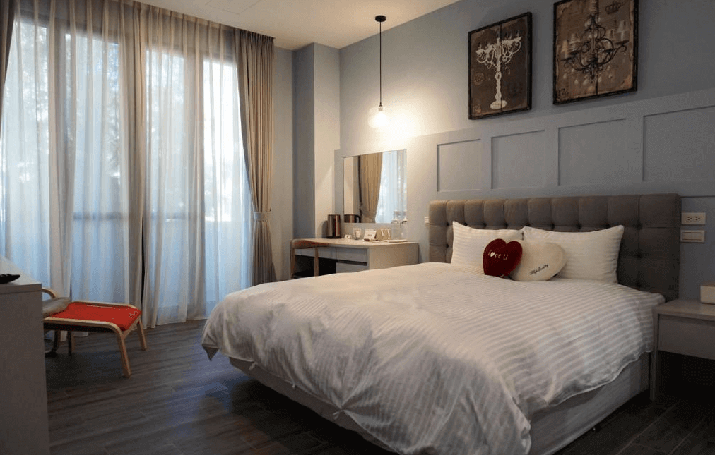 【水里住宿】恩典花園咖啡民宿典雅的臥室設計，牆面以柔和的藍色搭配簡約線條，床頭擺放有舒適的大床和裝飾枕。房間內設有化妝台和暖光吊燈，營造溫馨浪漫的住宿氛圍。
