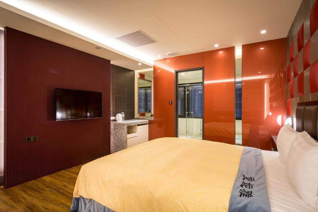 【北港住宿】愛妮雅汽車旅館的房內以紅色牆面搭配鏡面設計，增添視覺層次感，配有一張大床與壁掛式電視，整體空間感現代化且富有質感。
