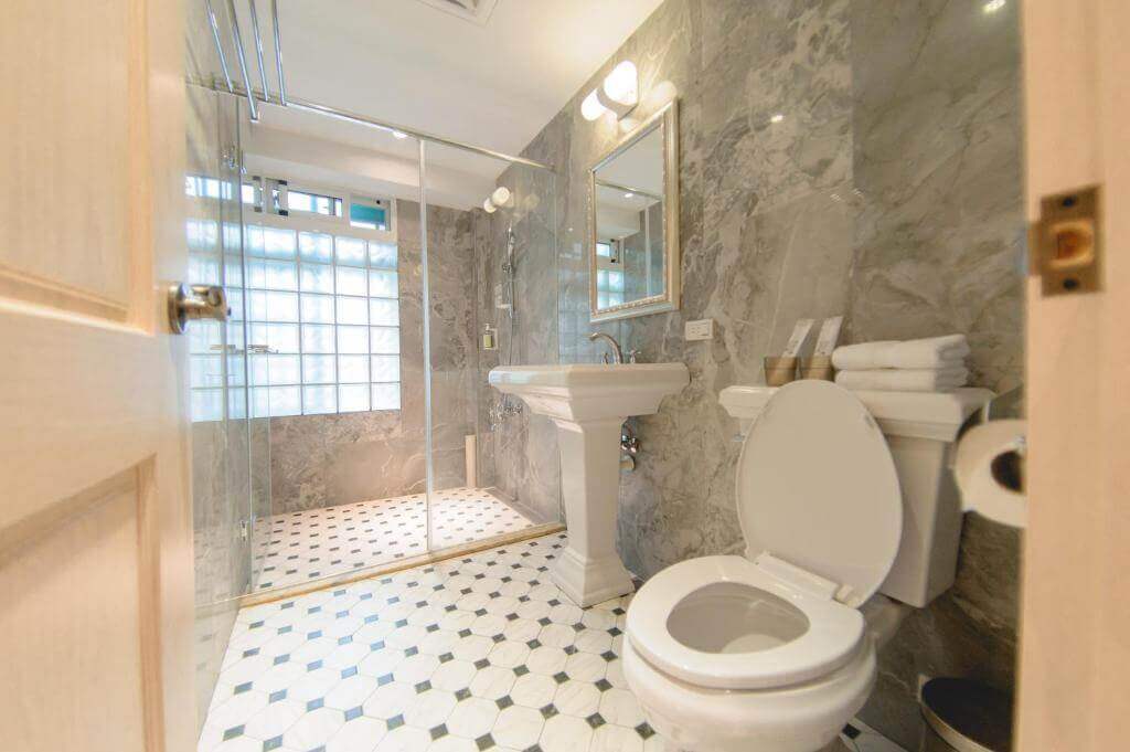 【北港住宿】暗街宅內民宿的浴室以大理石紋為主題設計，牆面與地板運用淺灰與白色搭配，配有簡約的白色洗手台和透明玻璃淋浴間，整體感覺清新明亮且具質感。