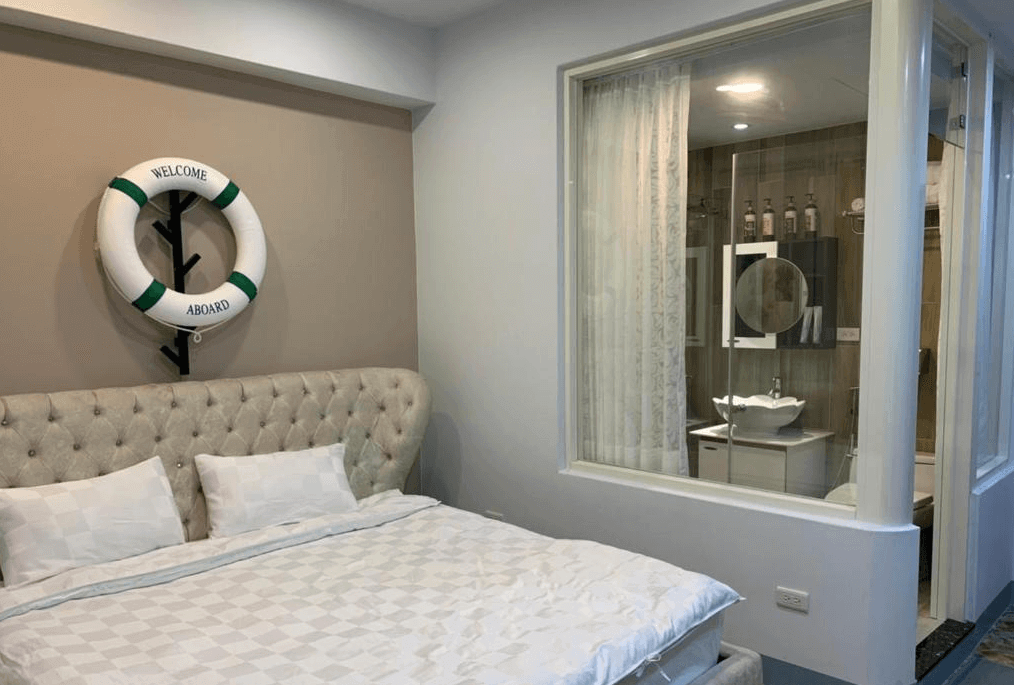 【水里住宿】月牙灣SUP民宿的房間設計以海洋為主題，牆上裝飾有救生圈，搭配柔軟的絎縫床頭板與白色床鋪，營造出溫馨的休閒氛圍。房間內還設有玻璃隔間，透視浴室的現代化設計。