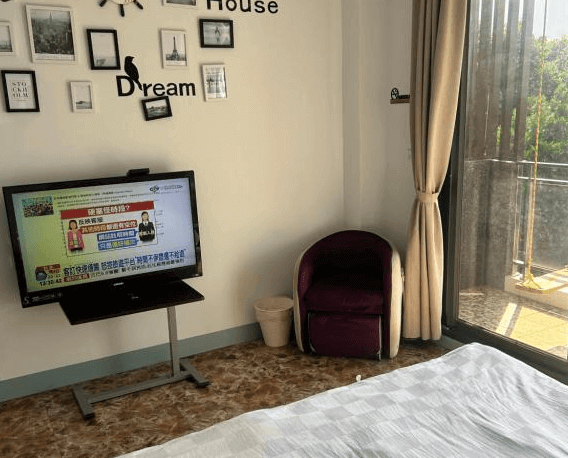 【水里住宿】月牙灣SUP民宿客房內設有簡單的擺設，如電視、舒適的單人座椅和通向陽台的落地窗，窗外景觀明亮開闊，牆上掛有裝飾性的照片與文字，增添房間的生活氣息。