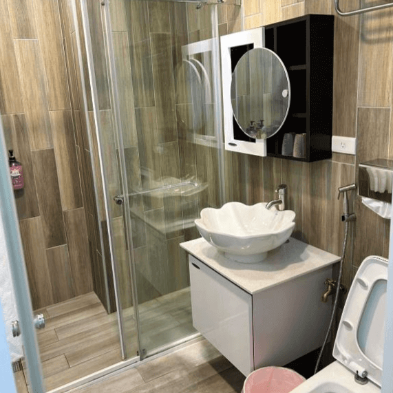 【水里住宿】月牙灣SUP民宿的浴室採用木紋磚設計，搭配貝殼造型的洗手台和乾濕分離的淋浴空間，設計既實用又具特色，營造出自然與現代感結合的風格。