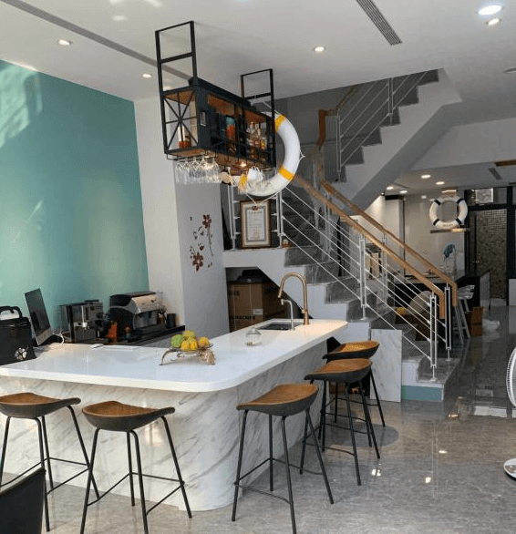 【水里住宿】月牙灣SUP民宿的公共區域設有大理石吧檯與高腳椅，牆面以清新藍色為主，整體風格簡約又富有現代感。樓梯區域與吊掛式酒架設計，提供一個舒適的交流與休憩空間。