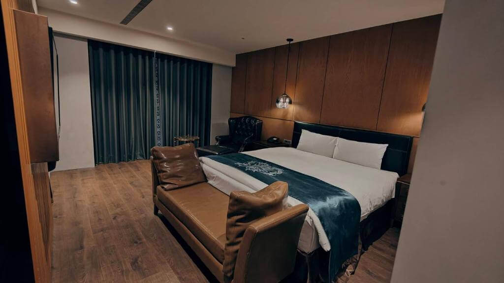 【北港住宿】朝聖酒店設有一張大床的私人房間，配以皮革沙發與深木色牆面，燈光柔和，營造出溫暖且私密的居住環境。