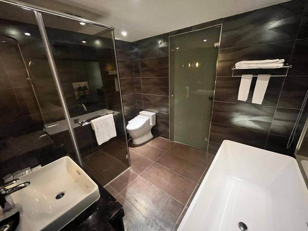 【北港住宿】朝聖酒店的浴室以深色瓷磚為基調，搭配乾濕分離設計，設有獨立浴缸與淋浴間，整體空間寬敞且高雅，適合追求放鬆的旅客使用。