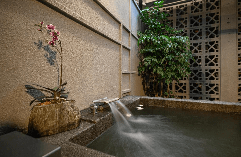 【礁溪住宿】東旅湯宿溫泉飯店-風華漾的私人溫泉池，池邊裝飾有植物與石造假山，水流從小型石製噴泉流入池中，營造出靜謐而放鬆的自然景致。