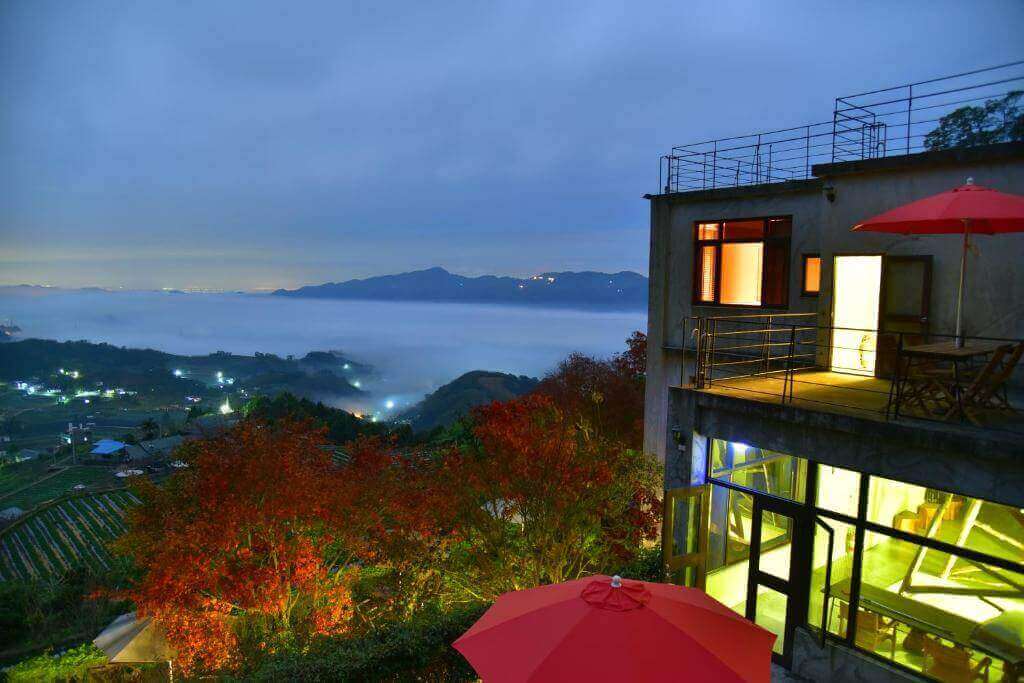 【大湖住宿】楓葉地圖的夜晚景色，山中建築物露台上燈光明亮，周圍點綴紅葉樹，遠處山巒被薄霧環繞，呈現如夢如幻的夜間景觀，營造浪漫氛圍。