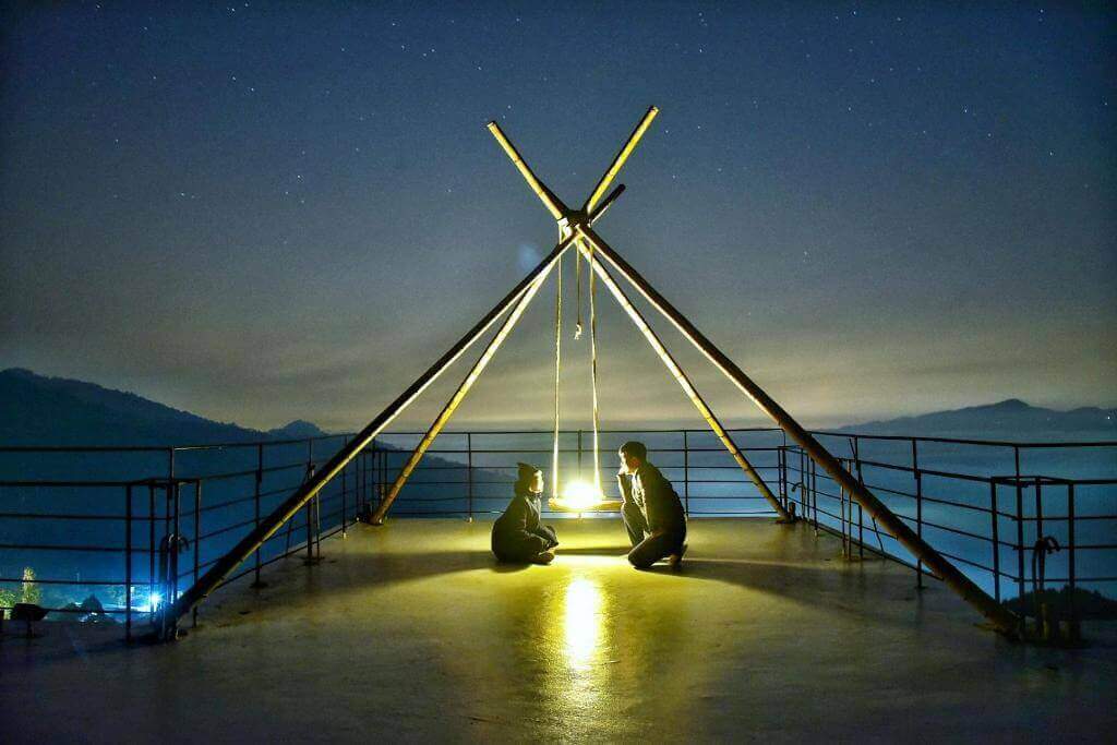 【大湖住宿】楓葉地圖的屋頂露台設有簡約木架與燈光，兩人坐在地板上仰望星空，遠處可見山巒與夜景，整體場景寧靜且充滿浪漫氛圍。