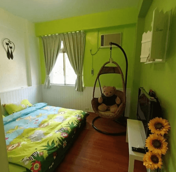 【水里住宿】水里河堤咖啡民宿充滿童趣的臥室設計，牆面採用鮮綠色塗料，搭配動物圖案的床單，散發歡樂氣息。房間內擺放有一個可愛的吊籃椅，搭配毛絨玩具，為家庭旅客帶來溫馨的感覺。