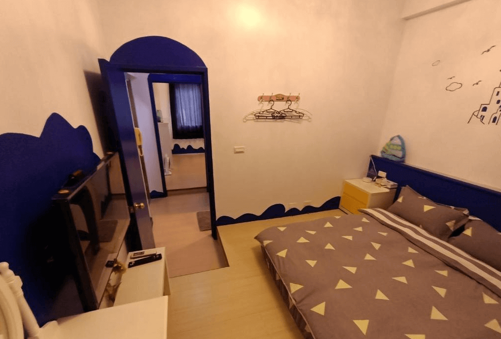 【水里住宿】水里河堤咖啡民宿的房間內採用藍白色調，牆上裝飾以波浪及簡約手繪圖案，呈現海洋主題風格。房間設有電視、簡單的收納架以及舒適的雙人床，營造輕鬆的住宿環境。