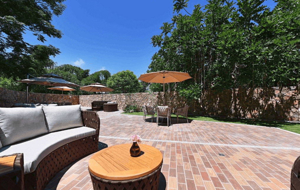 【水里住宿】水里福容徠旅的戶外庭園休息區，鋪設紅磚地面，配有舒適的藤椅與陽傘，周圍綠樹成蔭，提供旅客一個放鬆休憩的愜意場所。