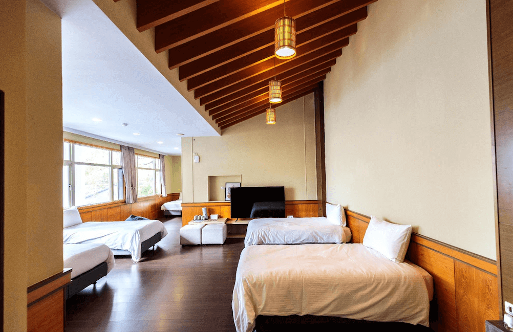 【水里住宿】水里里山村德川森態旅館的多床型家庭房，設計融入日式木質元素，搭配挑高天花板與懸掛燈飾，空間感十足。窗邊提供寬敞的休息區，讓旅客享受悠閒時光。