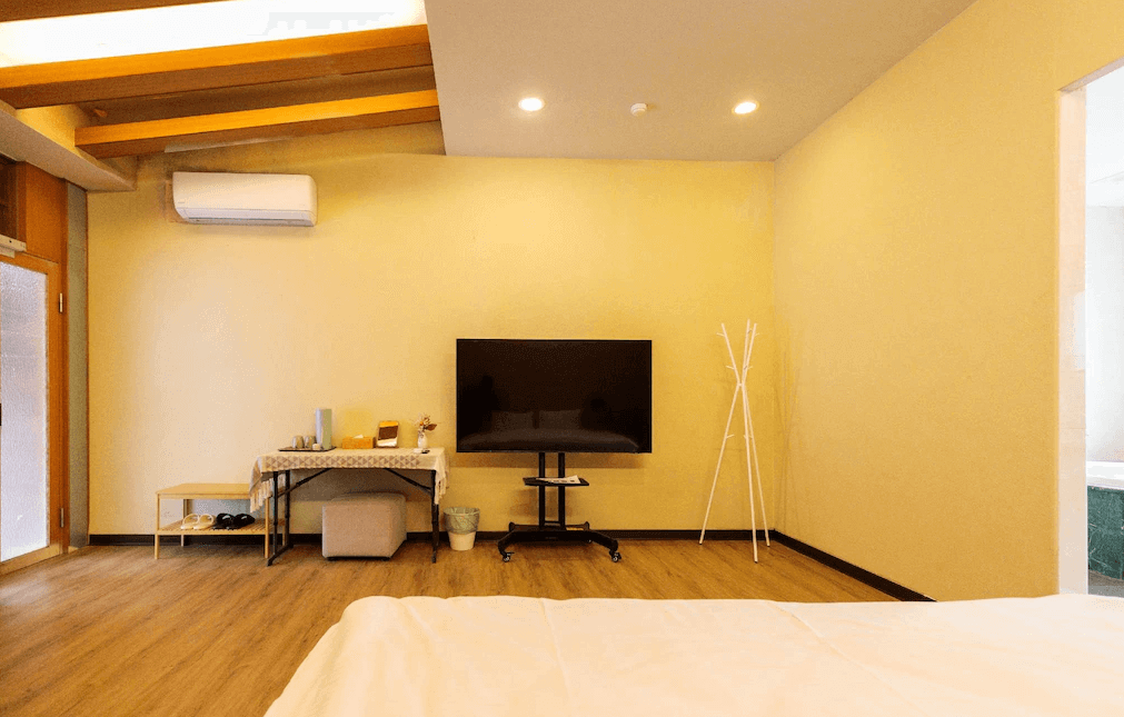 【水里住宿】水里里山村德川森態旅館的房間設計簡潔而實用，木質地板與黃白色牆面營造溫暖氛圍。電視牆與桌椅設置便利，空間寬敞，提供舒適放鬆的住宿體驗。