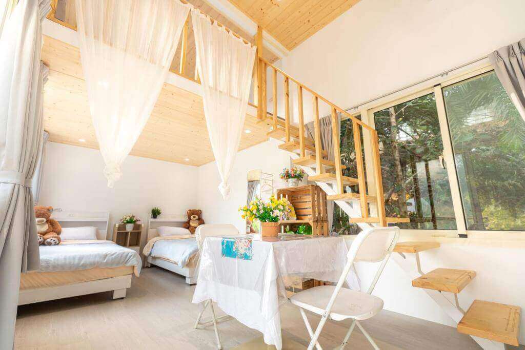 【大湖住宿】水頭人家生態美學民宿的房間內部採雙層結構設計，一樓有兩張單人床，搭配柔軟布簾與木質樓梯，桌上擺放鮮花裝飾，窗戶外可見綠意盎然的景色，整體氛圍溫馨明亮。