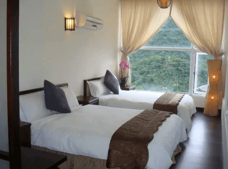 【烏來住宿】泉世界溫泉會館的房間內有兩張單人床，床頭背景牆設計簡約，配以柔和的窗簾和自然光線，窗外可欣賞山景。床上鋪有白色床單與深色裝飾毯，增添優雅氣息。