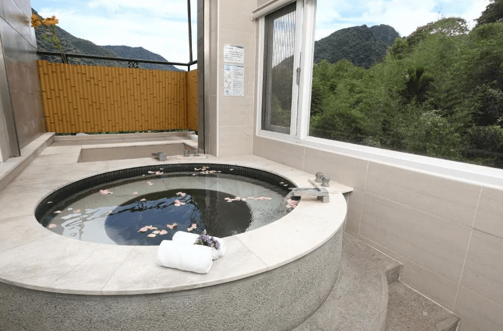 【烏來住宿】泉世界溫泉會館的私人溫泉泡湯區，圓形石材溫泉池內灑滿花瓣，窗外可見竹林與山景。整體設計簡約優雅，結合大自然的景致，提供極致放鬆的享受。