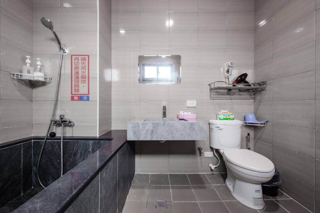 【大湖住宿】泉銘行館的浴室空間設計現代，灰色磁磚牆面搭配黑色大理石浴缸，配有淋浴設備與乾濕分離設計，並附有基本衛浴用品，整體乾淨實用。